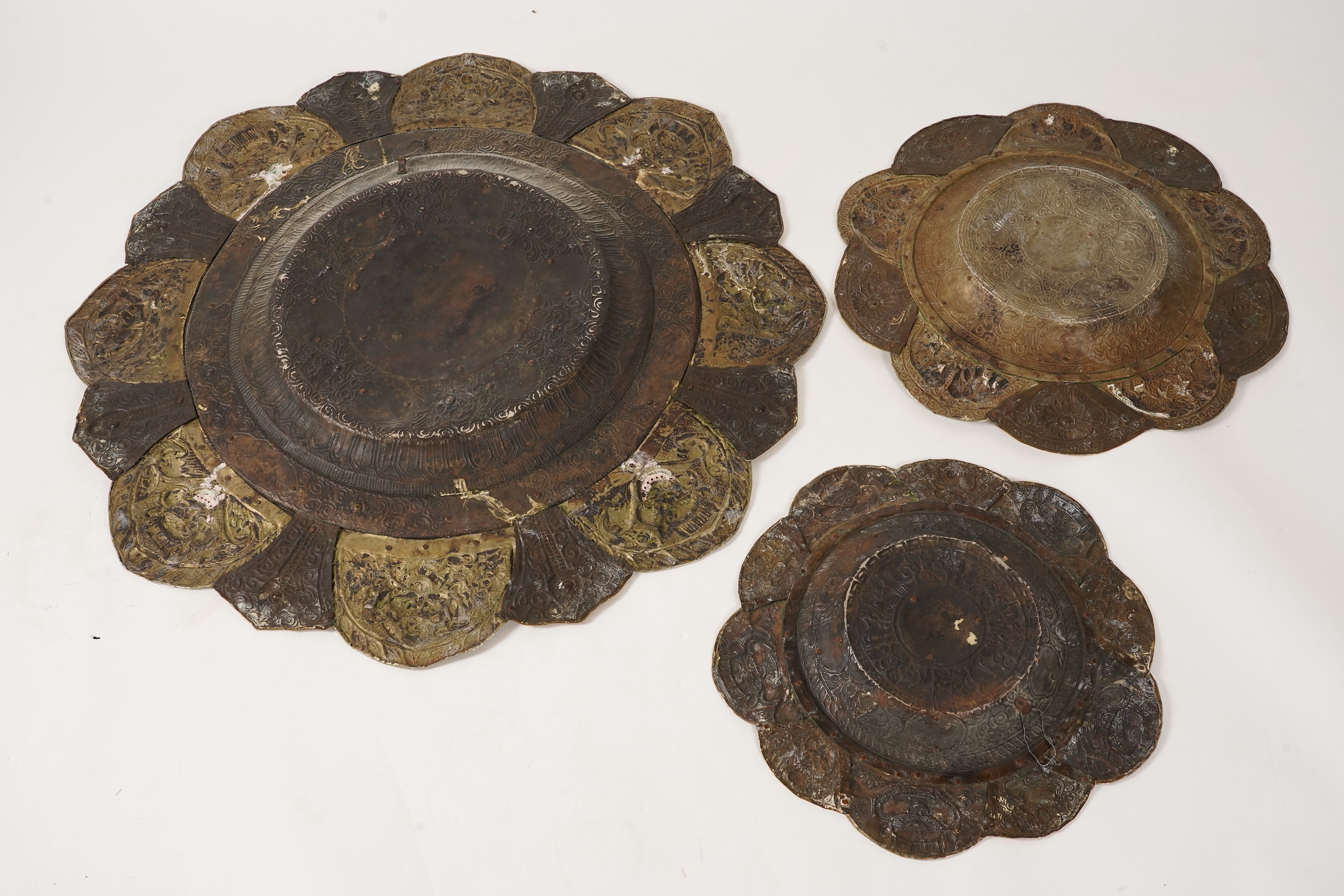 A graduated set of three Nepalese repoussé white metal and brass chargers, first half 20th century